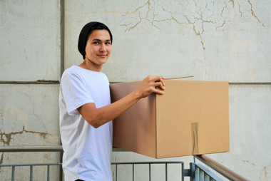 Am Foto ist Alkazar zu sehen. Der junge Mann siedelt mit seinem Karton gerade um. In seine erste eigene Wohnung, vermittelt und betreut vom Roten Kreuz Tirol