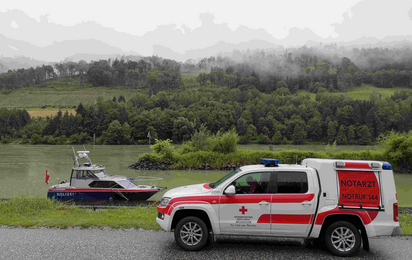 Notarzteinsatzfahrzeug parkt vor Donau, Schiff im Hintergrund