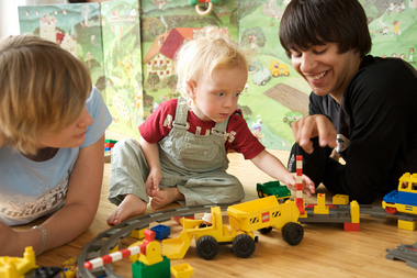 Babyfit 2009. Ausbildung (Kurs) zum Babysitter. Jugendliche/Teenager. Junge und Mädchen spielen mit Kleinkind am Boden mit Legosteinen und Spielzeugeisenbahn. Querformat.