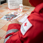 Man sieht einen Rotkreuz-Mitarbeiter der die Rotkreuzdose aus einer Tasche auspackt.