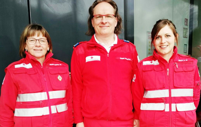 Gruppenfoto von drei Personen in Rotkreuz-Uniform vor einem Rotkreuz-Gebäude