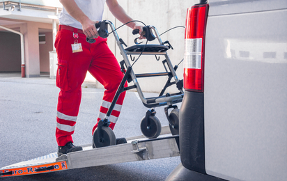 Ein Rotkreuz-Mitarbeiter lädt eine Gehhilfe in einen Transport Wagen ein.