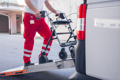 Ein Rotkreuz-Mitarbeiter lädt eine Gehhilfe in einen Transport Wagen ein.