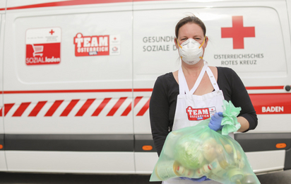 Eine Dame hält einen Sack mit Lebensmitteln hinter Ihr steht ein Auto mit dem Team Österreich Logo