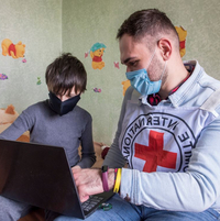 Ein Mitarbeiter des Roten Kreuzes zeigt einem kleinen Buben etwas auf dem Laptop