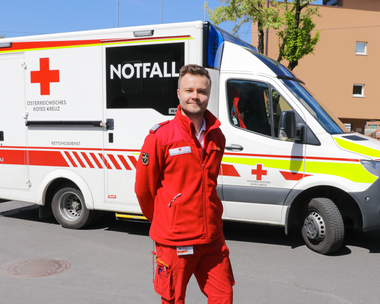 Das Bild zeigt den Rettungsmediziner Thomas vor einem Notfallwagen der Rotkreuz-Bezirksstelle Graz-Stadt.