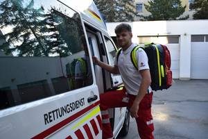 Nico Fritz - Zivildienstleistender im Rettungs- und Krankentransportdienst hat einen Notfallrucksack am Rücken und steigt gerade in einen Rettungswagen ein. Er lächelt dabei in die Kamera.