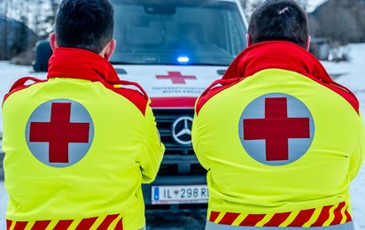 zwei Sanitäter stehen mit dem Rücken ins Bild und in ihren Uniformen vor einem rettungsauto