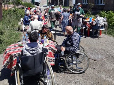 Mehrere Personen in Rollstühlen sitzen in der Sonne vor einem Gebäude