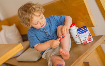 Erste Hilfe bei Kindernotfällen. Kind verarztet die Wunde am Bein mit einem Pflaster