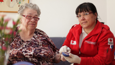 Eine Rotkreuz-Mitarbeiterin misst im Rahmen der Hauskrankenpflege bei einer Klientin den Blutzucker.