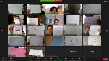 Die Teilnehmerinnen und Teilnehmer eines Webinars halten ein Stück Papier mit einem gemalten lachenden Gesicht in die Kamera