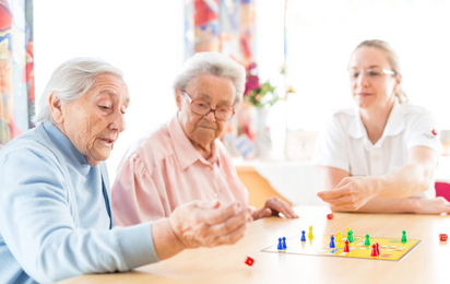 Zwei Seniorinnen und eine Rotkreuz-Mitarbeiterin spielen ein Brettspiel.