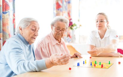 Zwei Seniorinnen und eine Rotkreuz-Mitarbeiterin spielen ein Brettspiel.