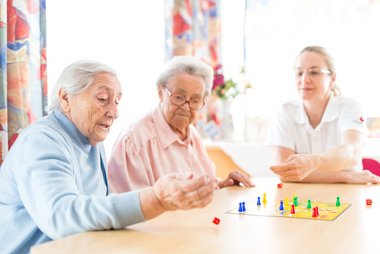 Zwei Seniorinnen und eine Rotkreuz-Mitarbeiterin spielen ein Brettspiel.