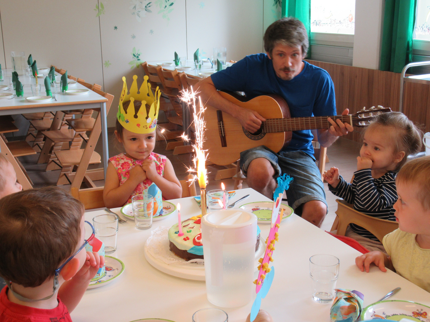 ein Kindergärtner - ein junger Mann, spielt auf der Gitarre den Kindern im Kindergarten vor