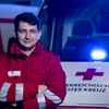 Zwei Zivildiener stehen vor einem Rettungswagen mit Blaulicht.