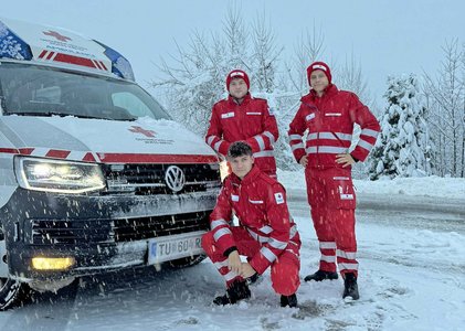 Drei Sanitäter stehen in einer tief winterlichen Landschaft vor einen Krankentransportwagen.