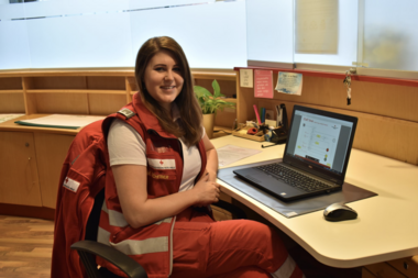 Michaela Scheiber sitzt in Rotkreuz-Uniform in einem Büro vor ihrem Notebook.