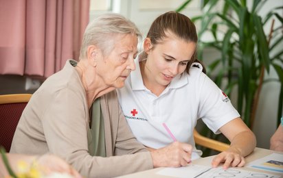 Eine Rotkreuz-Mitarbeiterin und eine ältere Dame arbeiten gemeinsam Übungsblätter durch