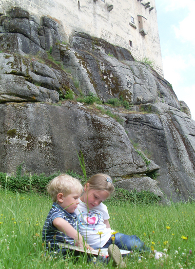 Zwei Kinder sitzen in der Wiese vor der Kinderburg Rappottenstein und lesen ein Buch.