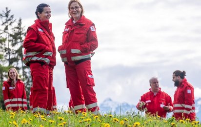 Eine Gruppe von 6 Rotkreuz-Mitarbeiterinnen stehen in Uniform in einem grünen Feld mit Löwenzahn