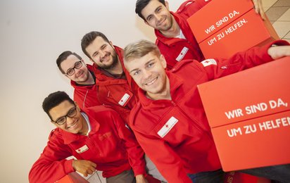 Fünf junge Männer in Rotkreuz-Uniform halten einen Würfel aus Karton mit der Aufschrift "Wir sind da, um zu helfen". Das ist der Leitsatz des Roten Kreuzes