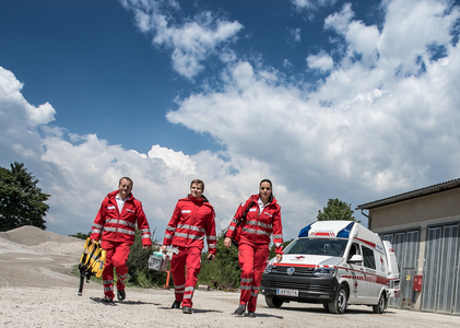 Drei Rettungssanitäter_innen gehen vom Rettungsauto auf die Kamera zu.