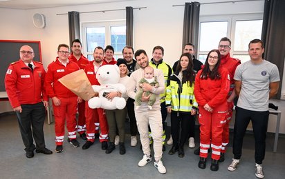 Gruppenfoto der Lebensretter:innen, des Elternpaars und der kleinen Mara