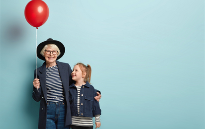 Innenaufnahme von modischen älteren Frau umarmt kleines Kind, genießen Sie die Zeit zusammen, feiern ersten Tag in der Schule, halten Luftballon, Pose über blauen Hintergrund mit leeren Raum auf der rechten Seite