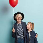 Innenaufnahme von modischen älteren Frau umarmt kleines Kind, genießen Sie die Zeit zusammen, feiern ersten Tag in der Schule, halten Luftballon, Pose über blauen Hintergrund mit leeren Raum auf der rechten Seite