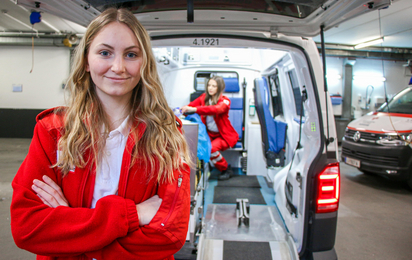 Eva steht vor der offenen Heckklappe eines Rettungsautos.