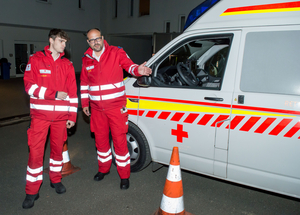 Gerald Muhr - Bezirksausbildungsleiter für Sichere Einsatzfahrer - weist einen jungen Mitarbeiter in Ausbildung in das richtige Einparken eines Rettungswagens ein. Beide tragen Rotkreuz-Einsatzuniform und stehen vor einem Rettungswagen.