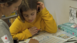 Ein Mädchen lernt gemeinsam mit einer Rotkreuz-Mitarbeiterin für die Schule