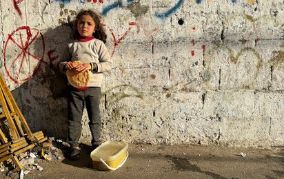 Mädchen in Gaza steht an einer Wand und hält Brot in der Hand