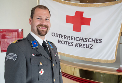 Ing. Christoph Berghofer - Bezirksstellenleiter - trägt seine Ausgangsuniform und steht vor einer Rotkreuz-Standarte.