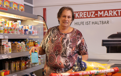 Eine Frau steht im Rotkreuz-Markt vor der Kühlvitrine und wählt mit Bedacht, Lebensmittel aus.