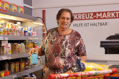 Eine Frau steht im Rotkreuz-Markt vor der Kühlvitrine und wählt mit Bedacht, Lebensmittel aus.