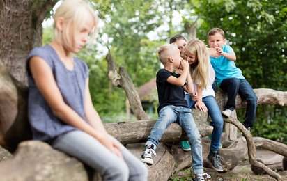 Ein traurig wirkendes Kind sitzt abseits einer Gruppe mit lachenden Kindern