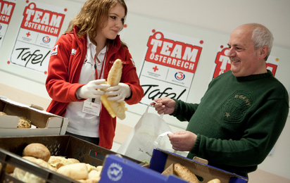 Auf dem Bild eine freiwillige die gerade Brot an einen Herren ausgiebt