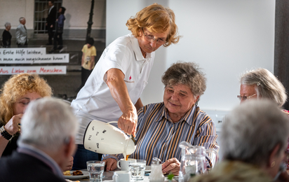 Eine Rotkreuz-Mitarbeiterin schängt den Senior_innen Kaffee ein.