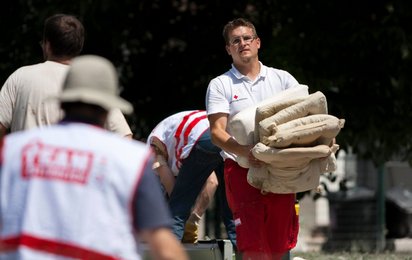 Hochwasser  das Rote Kreuz und Team Österreich sind im Einsatz. Ein Rotkreuz-Mitarbeiter trägt mehrere Sandsäcke.