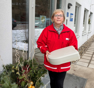 Helga Stadt mit Essen auf Rädern-Box vor der Dienststelle