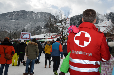 Ein Rotkreuz-Mitarbeiter in roter Uniform hält ein Kind in den Armen.