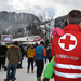 Ein Rotkreuz-Mitarbeiter in roter Uniform hält ein Kind in den Armen.