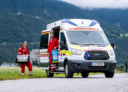 Die zwei Rettungssanitäterinnen des Roten Kreuzes Tirol stehen mit ihrem Rettungswagen auf einer Seitenstraße bei Telfs im Feld und laden gerade ihre Notfalltasche aus