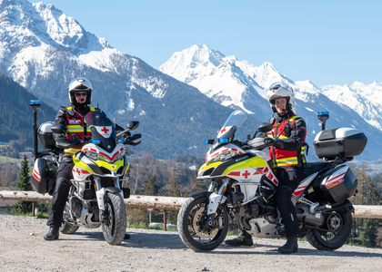 Jan Reiter und sein Kollege in der Rotkreuz-Motorradeinsatzuniform sowie ihre Einsatzmotorräder posieren vor der traumhaften Tiroler Bergkulisse