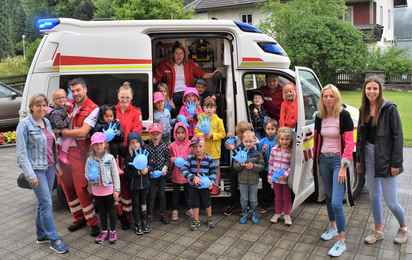 Gruppenfoto Rettungswagen, Sanitäter:innen und die Kinder des Kindergarten Kirchbach im Bezirk Hermagor.