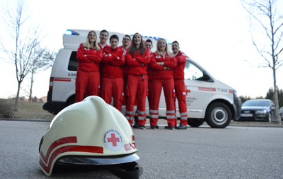 Rettungsdienstmitarbeiter der Bezirksstelle St. Veit posieren vor einem Rettungswagen. Im Vordergrund liegt ein Einsatzhelm.