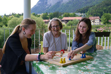 Am Bild spielen zwei junge Damen mit einer Älteren Dame Mensch ärgere Dich nicht. Es ist dies ein Projekt des Jugendrotkreuzes, bei dem junge Menschen ältere unterstützen